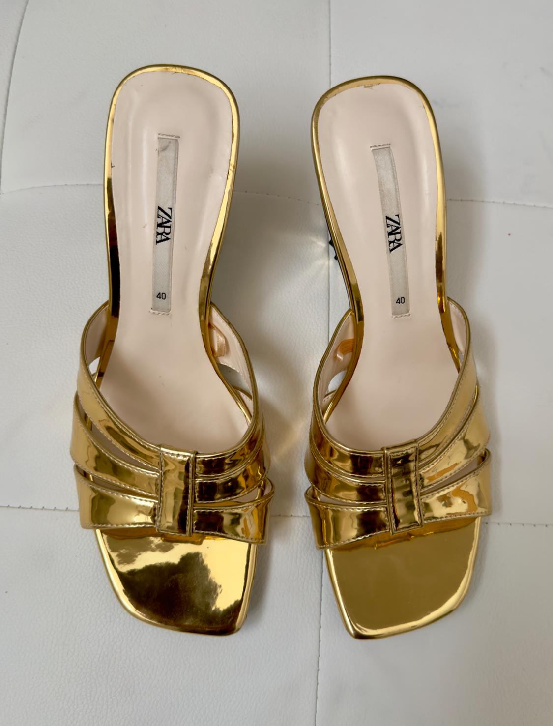 Gold low-heeled sandals with a criss-cross strap design on a white background. Visible label with brand and size 40.