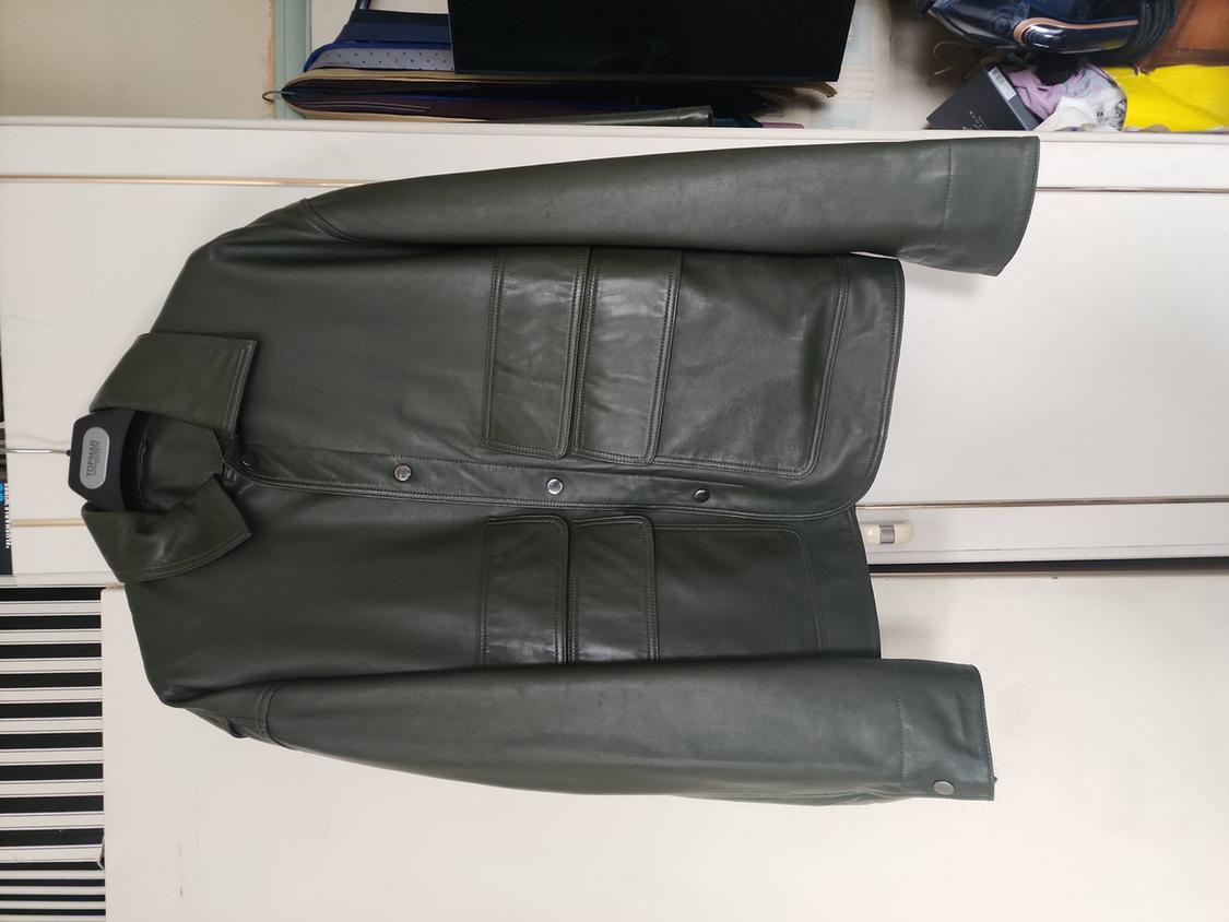 Dark green faux leather jacket with four pockets, hanging on a hanger with the text TOPMAN in front of a white wardrobe.
