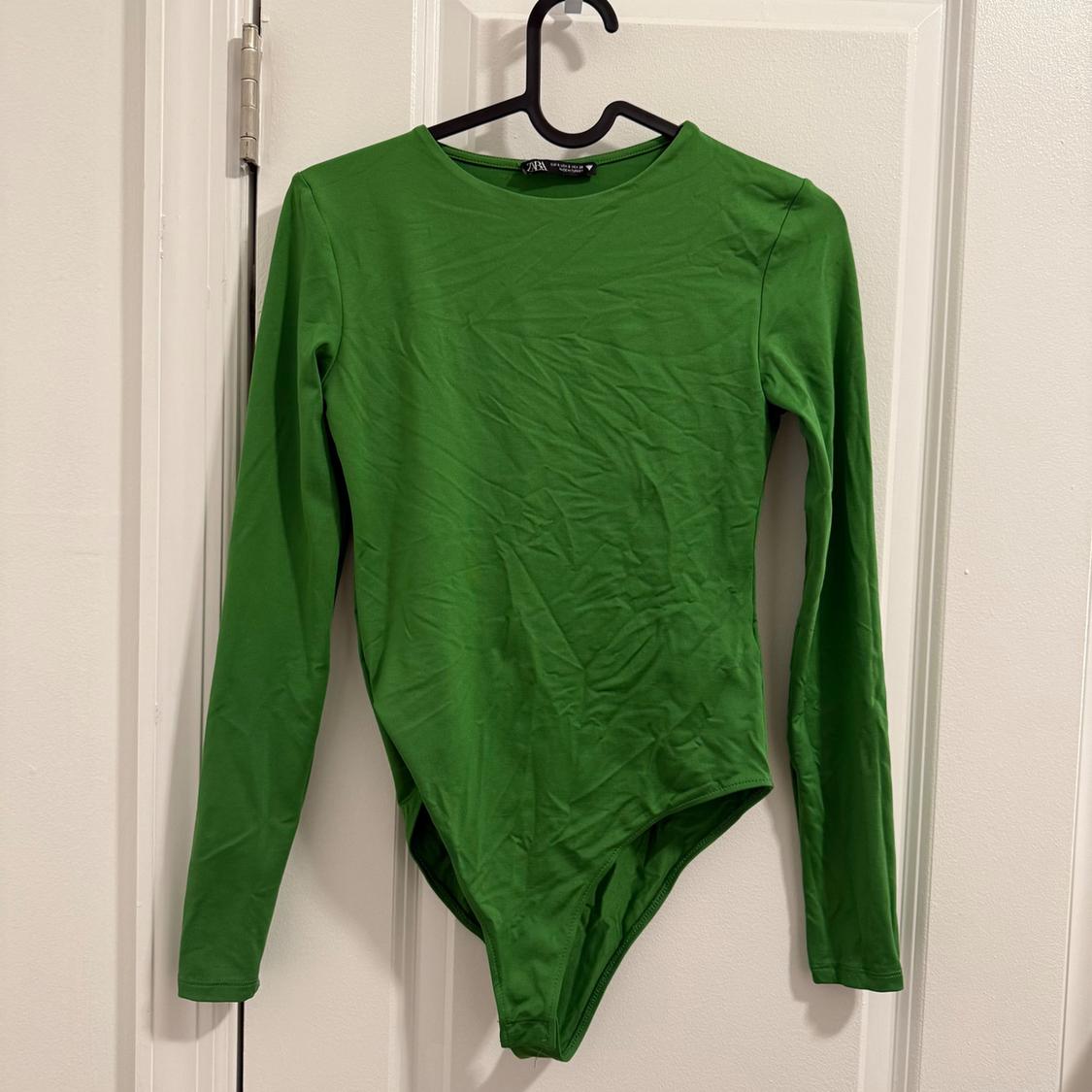 Green long-sleeved bodysuit hanging on a black hanger over a white door.