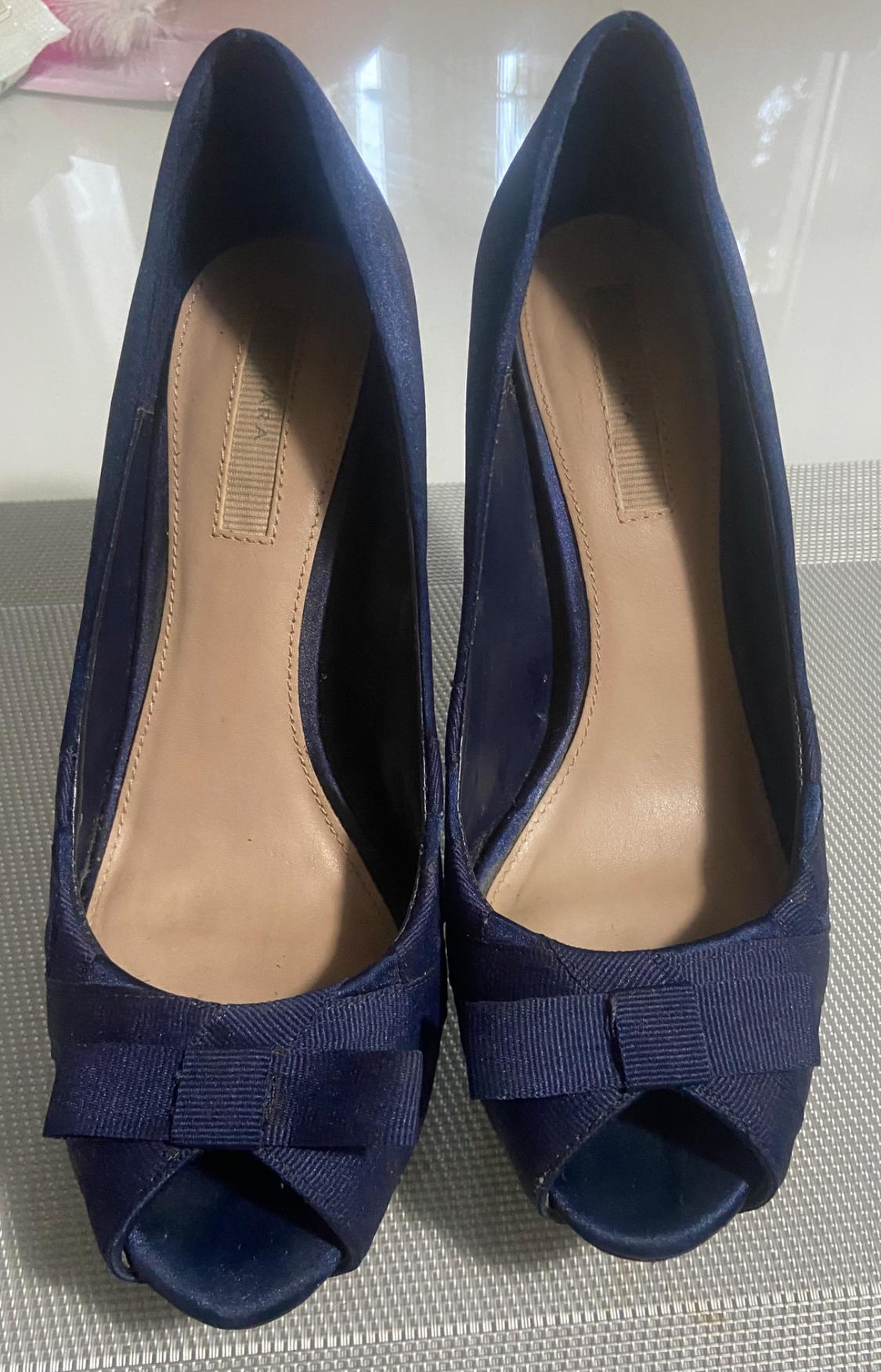 Front view of navy blue high-heeled shoes with a decorative bow and an open-toe design.