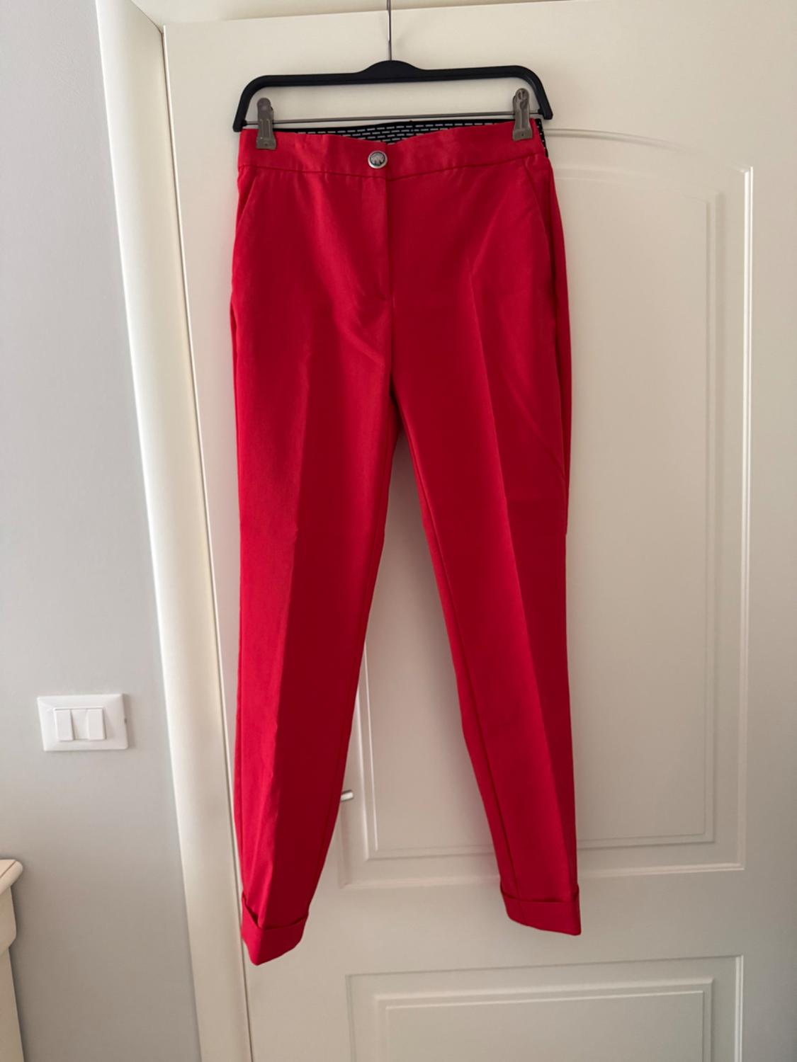 Red trousers hanging on a black hanger over a white door. Indoor setting with natural light.