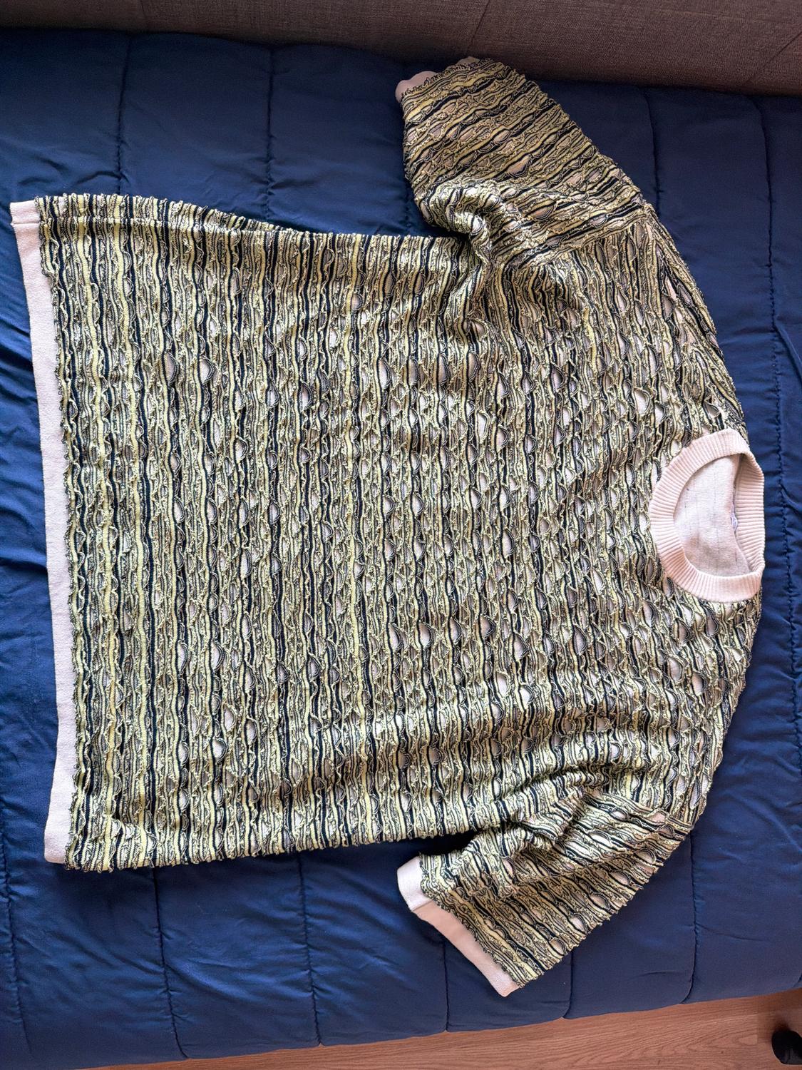 Short-sleeved jumper with a textured pattern in beige and black tones, on a blue quilt.