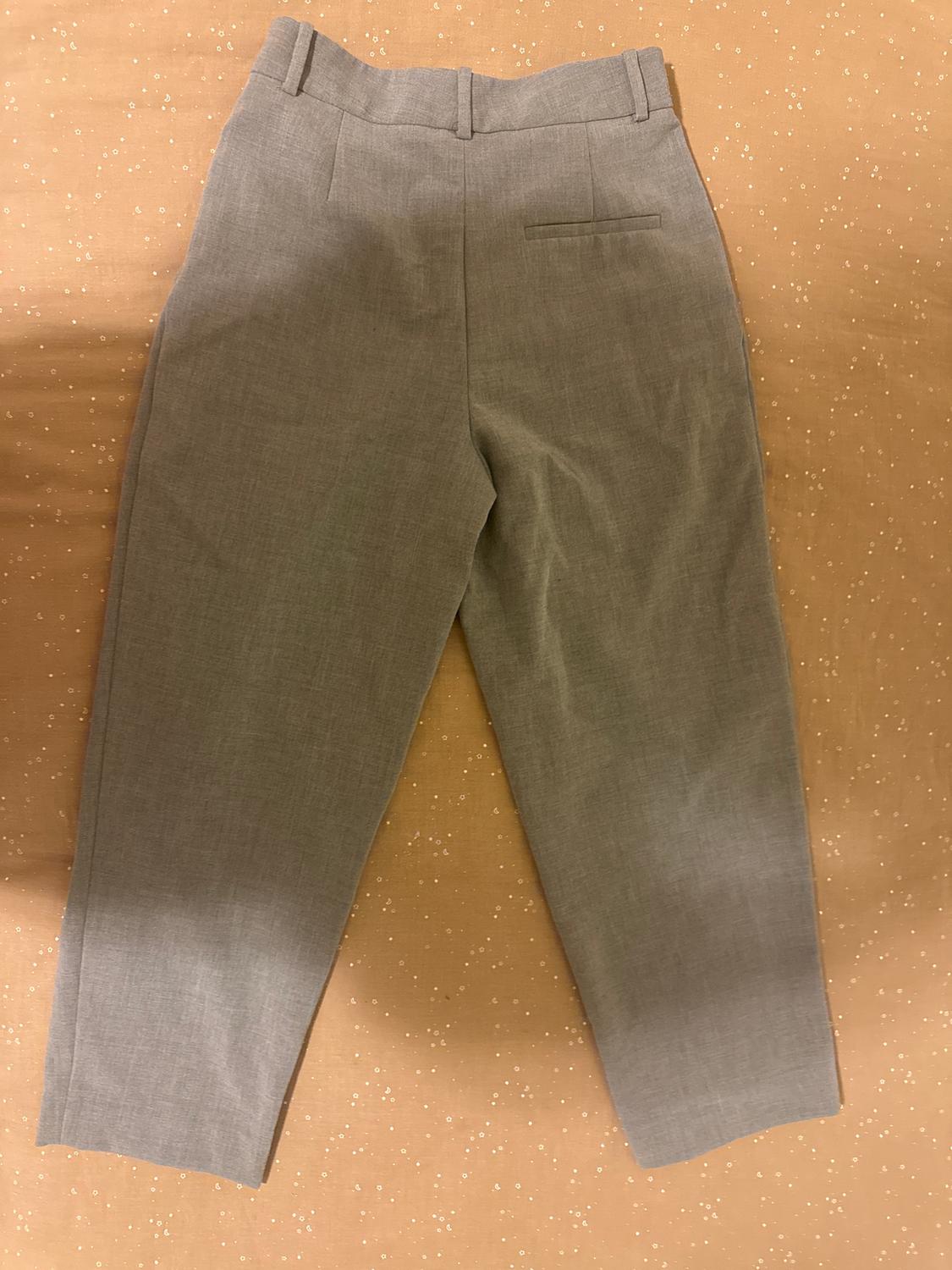 Light grey fabric trousers on a beige background with small white dots. Classic design with back pockets and belt loops.