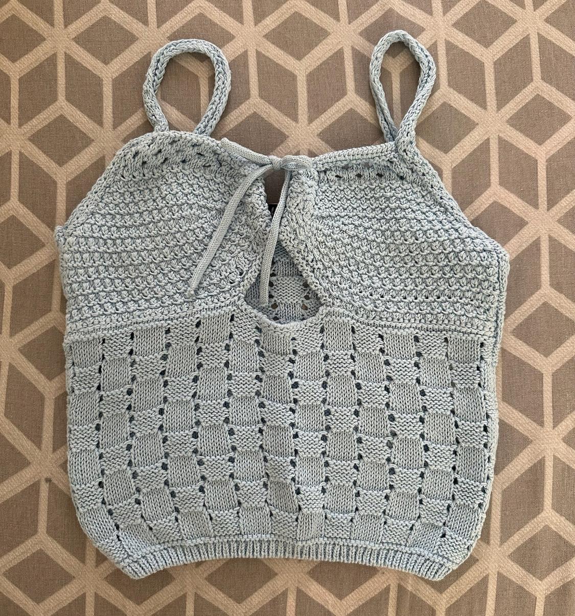 Light blue textured knit top with thin straps, bow and cut-out detail at the neckline, against a brown geometric background.