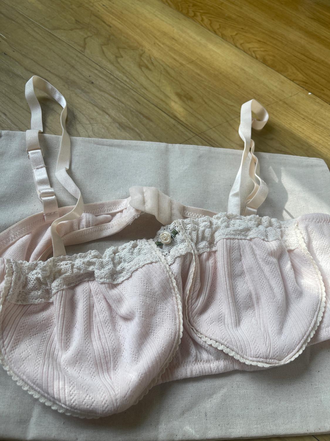 Light pink bra with white lace and floral detail, on beige fabric and a light wood background.