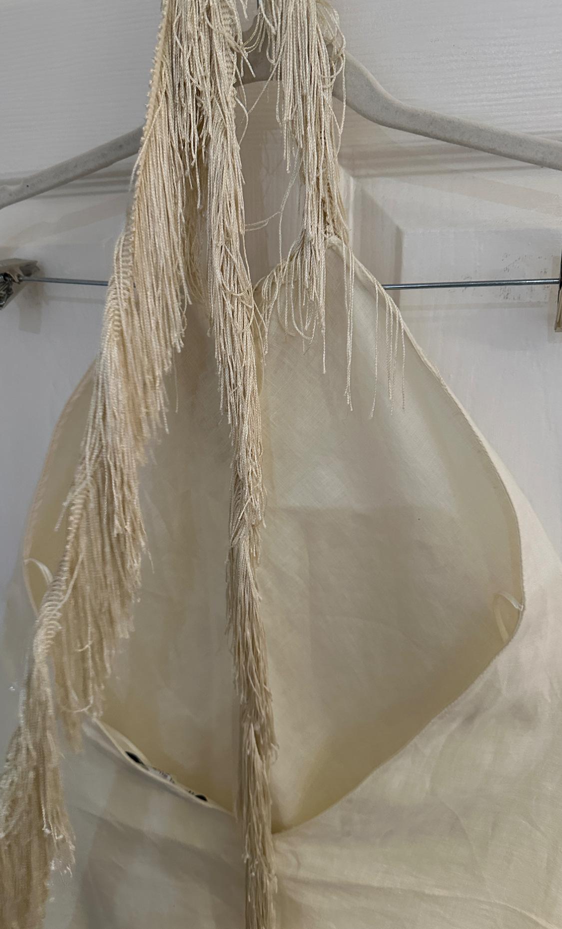 Cream-coloured garment with straps made of long fringing, hanging on a metal hanger in front of a white door.
