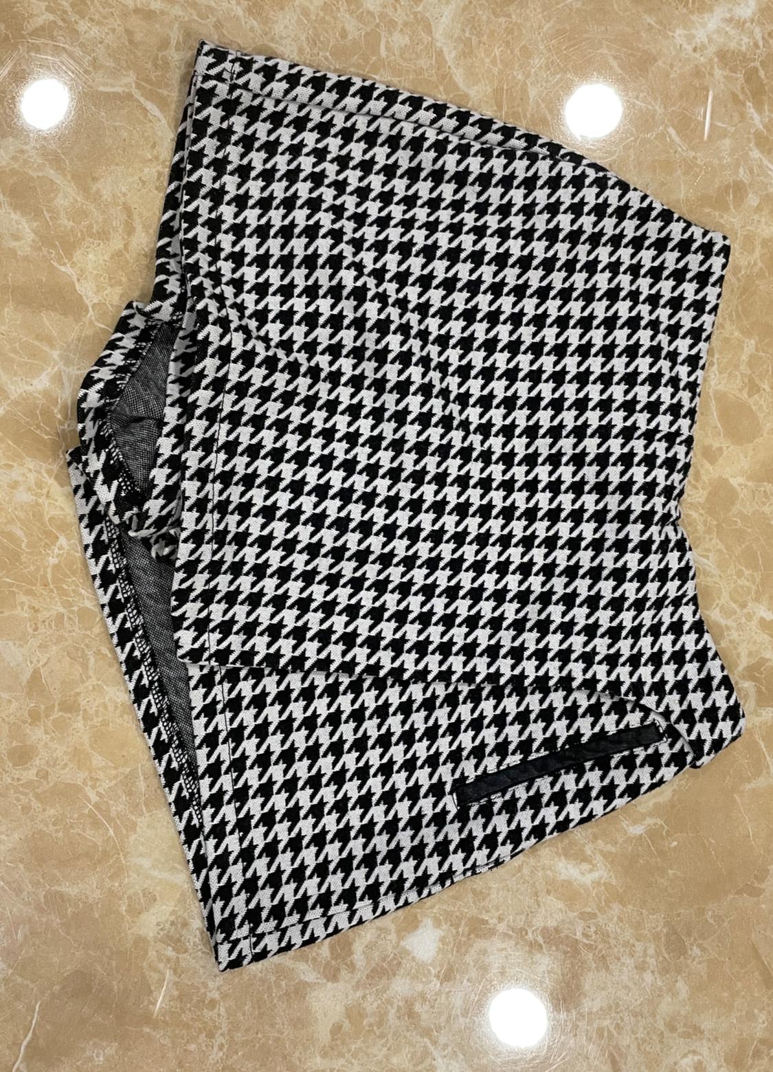 Folded garment with a black and white houndstooth pattern on a beige marble surface with light reflections.