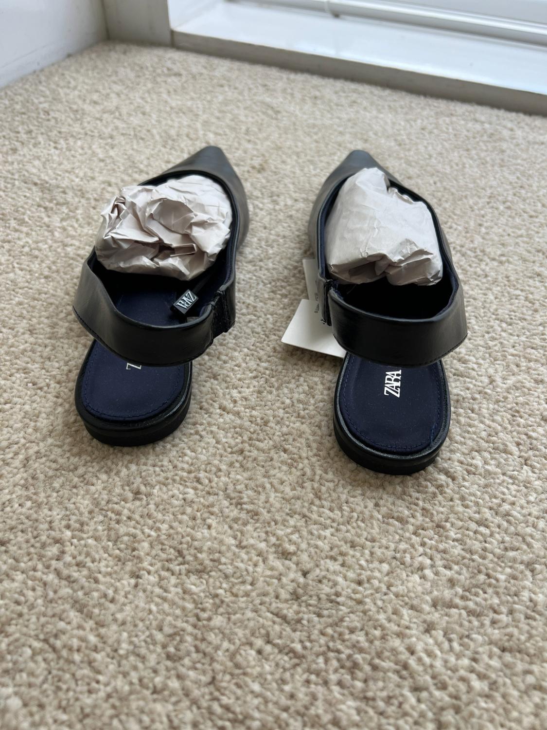 Black pointed-toe slingback shoes with stuffing inside, on a beige carpet. ZARA is visible on the insoles.