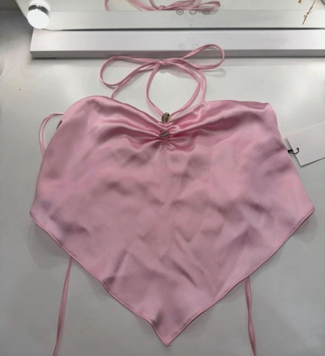 Satin pink halter neck top, with front gathered detail and pointed hem, on a white surface in front of a lighted mirror.