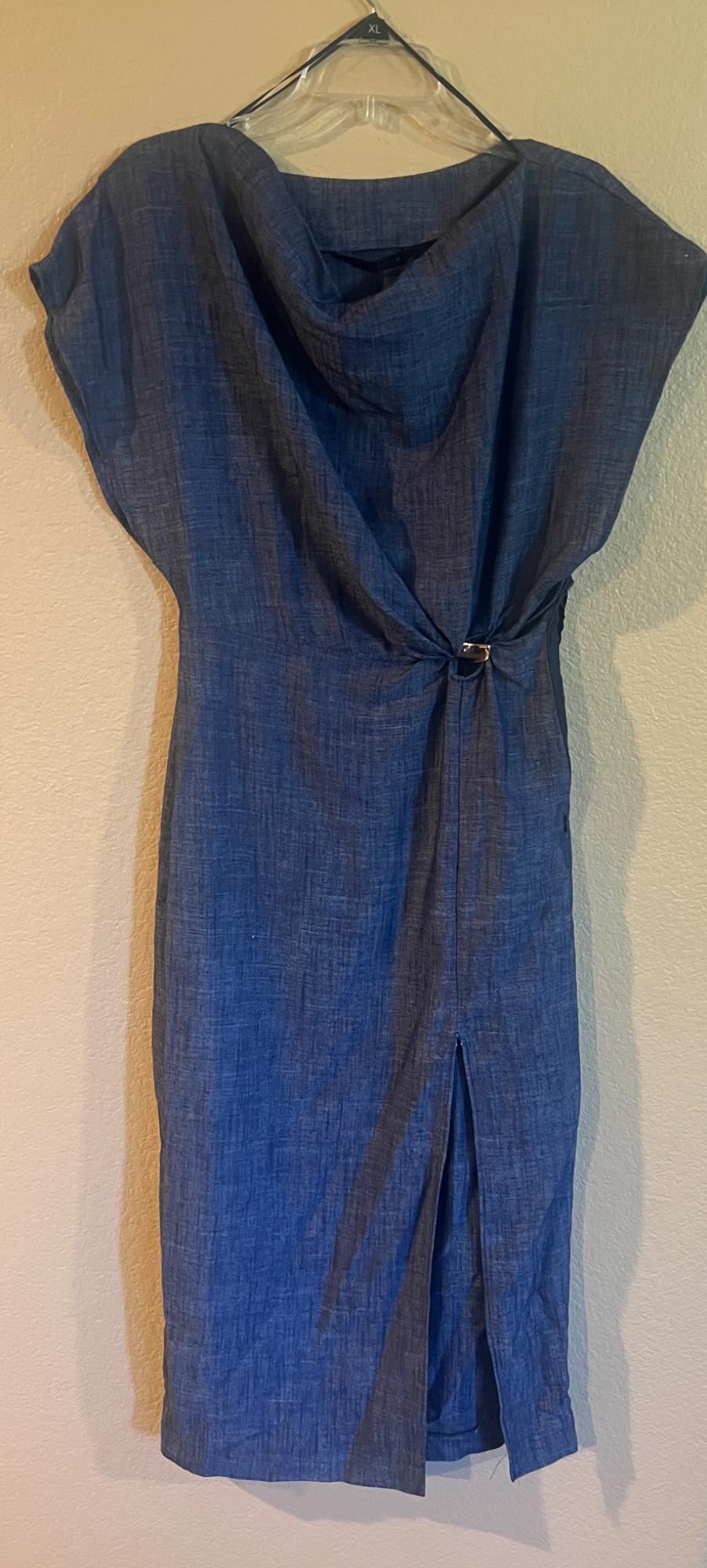 Blue dress made of lightweight fabric hanging on a transparent hanger. Design with pleats and a rear vent, on a beige background. Size XL visible.