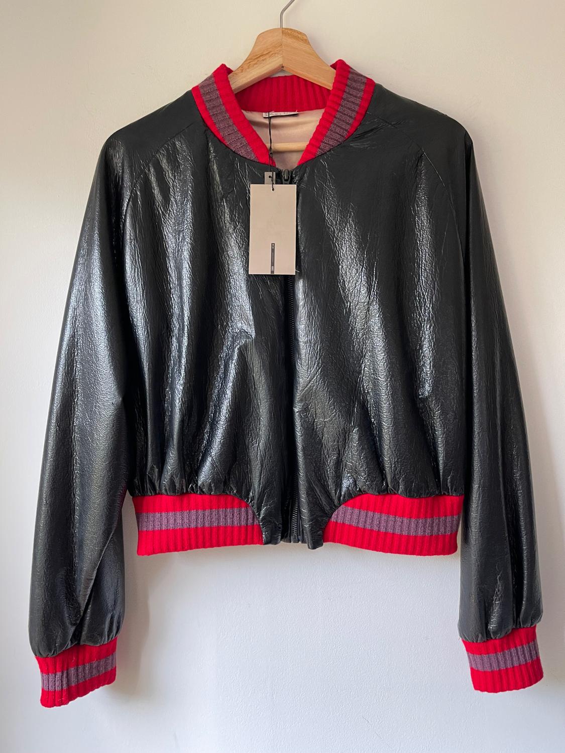 Shiny black jacket with red and grey striped collar, cuffs and waistband, hanging on a wooden hanger. Label visible.