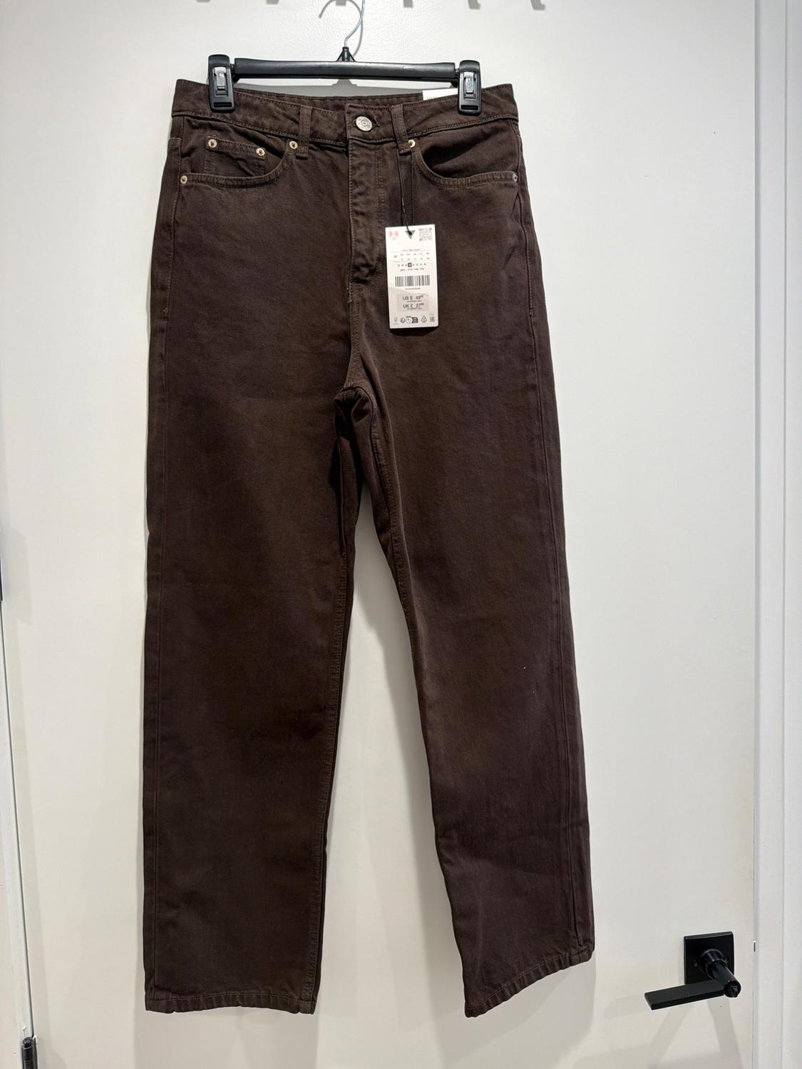 Brown pants hanging on a black hanger over a white door. Visible tag with product details.