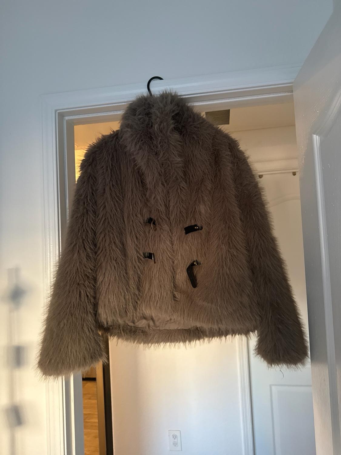 Light brown fur jacket hanging on a black hanger in the frame of a white door inside a house.