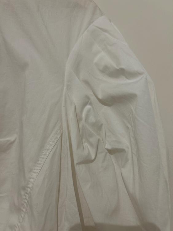 Detail of a crumpled white shirt, showing the shoulder seam and sleeve against a light background.