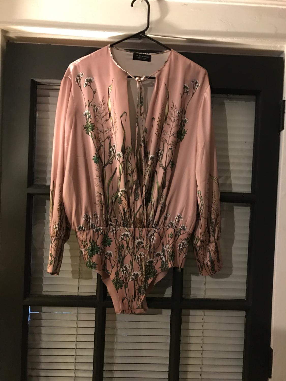 Front view of a pink bodysuit with long sleeves and a floral print.