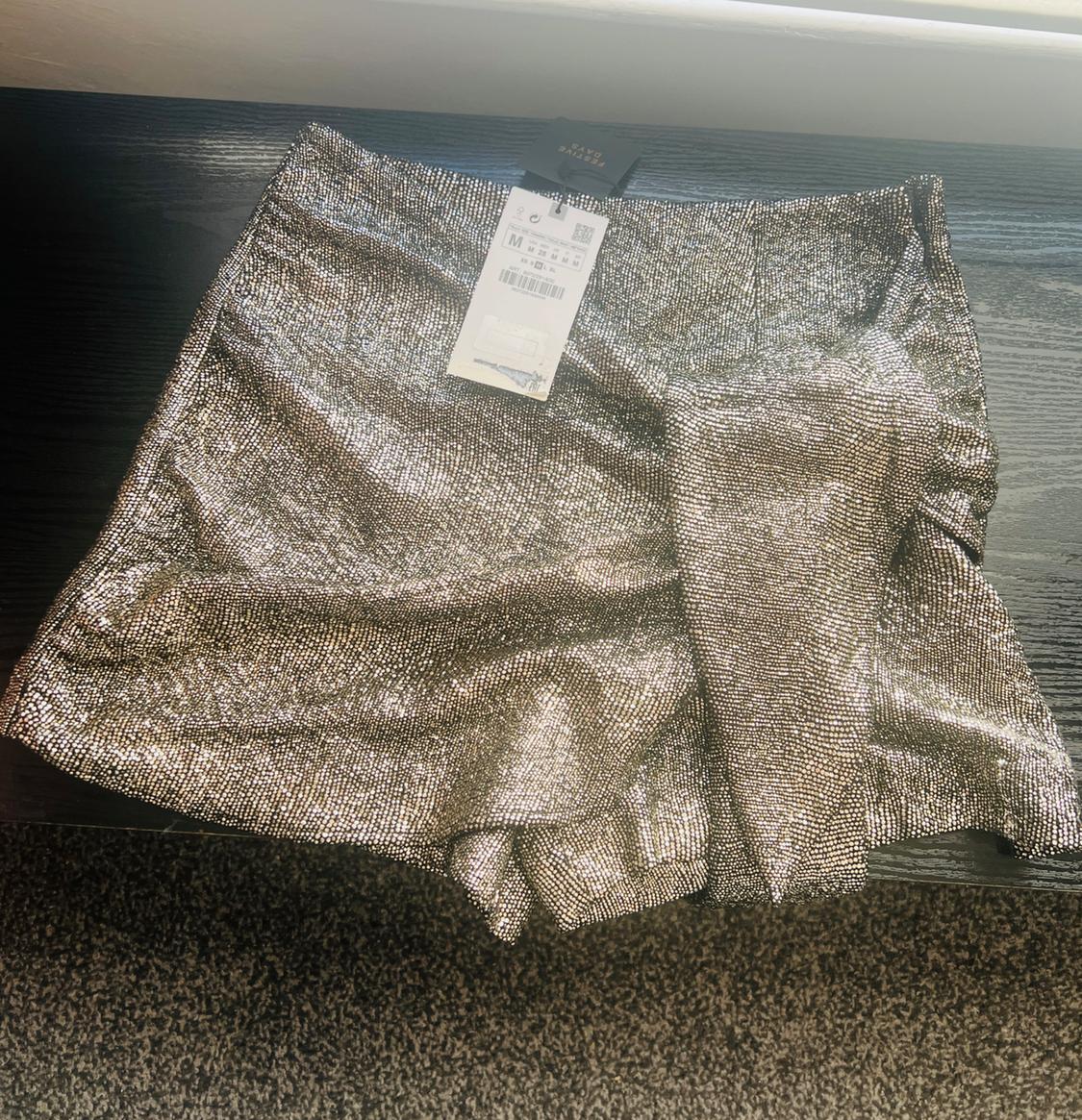 Shiny silver shorts on a dark surface, with a visible label showing size M and a barcode.