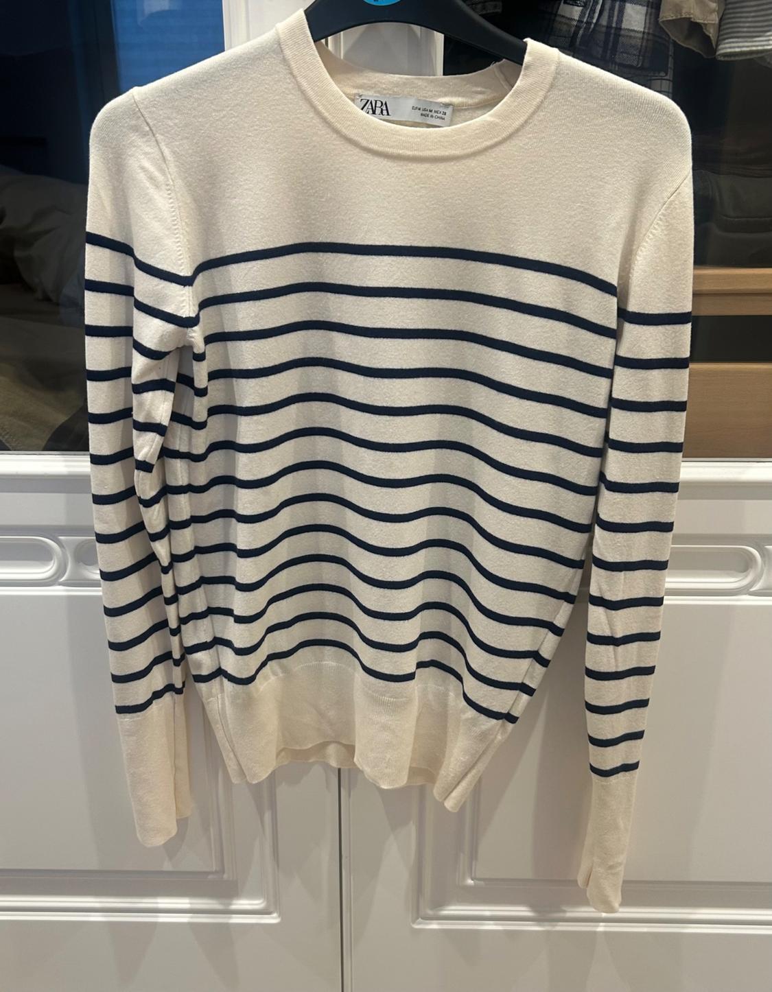 Navy and white striped jumper hanging on a black hanger in front of a white door. Visible label: Zara.