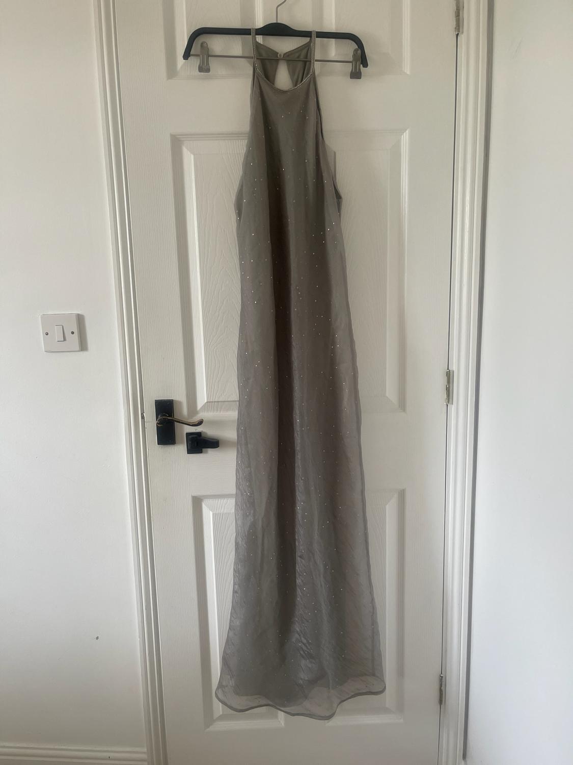 Long grey dress with a halter neck and subtle shimmer, hanging on a coat hanger over a white door.