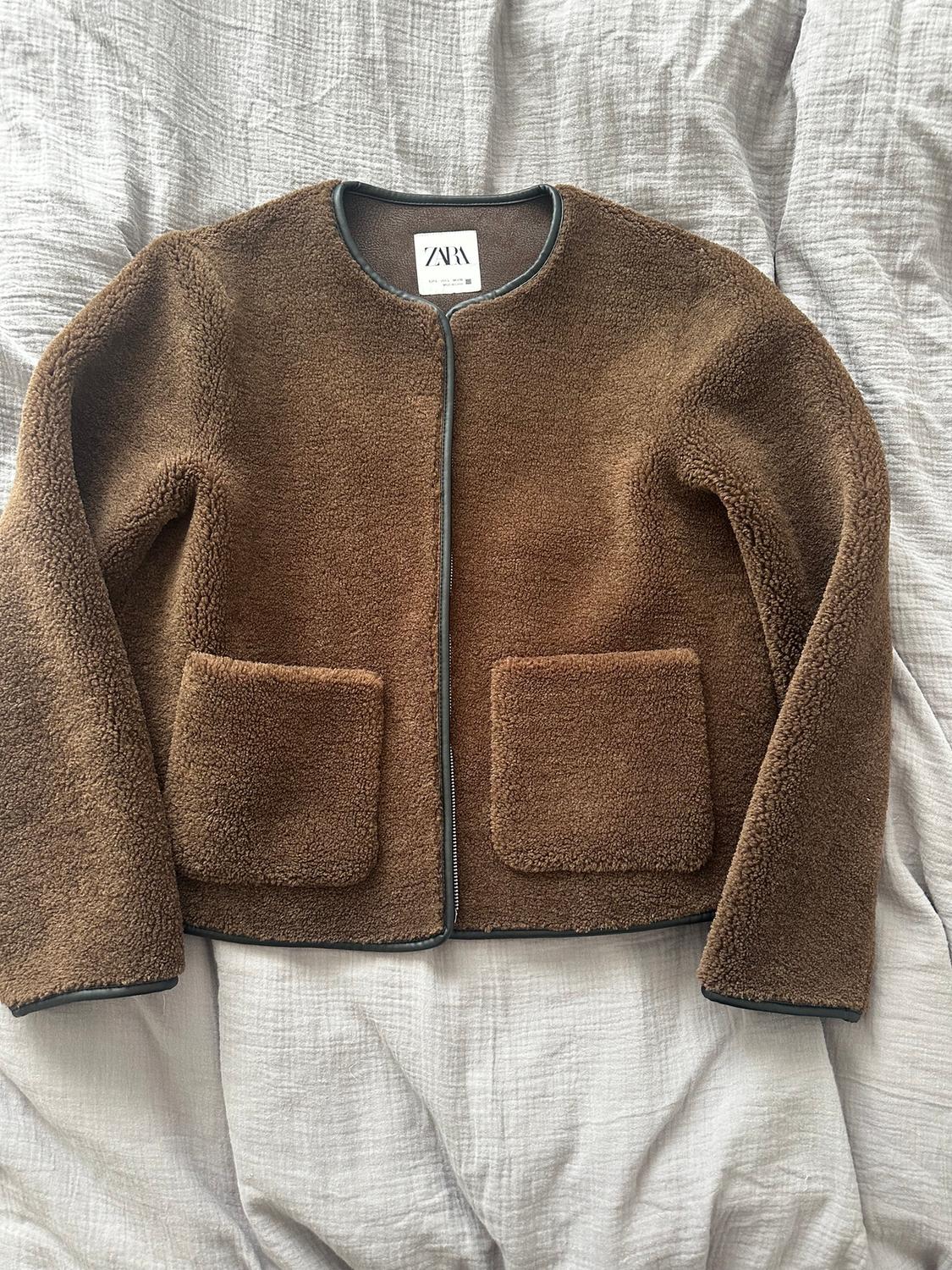 Soft-textured brown jacket with two front pockets, on a grey surface. Visible label with the text "ZARA".