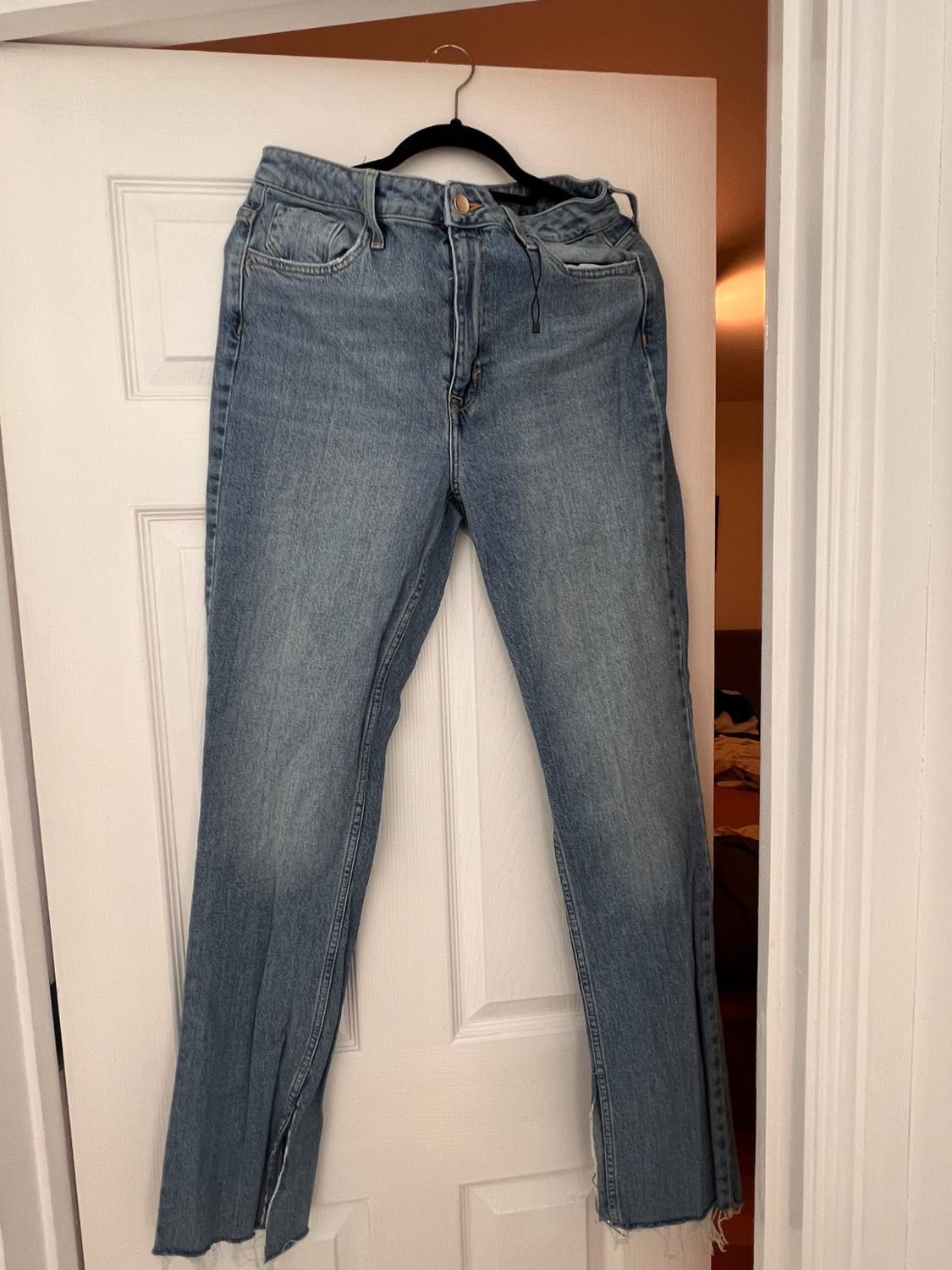 High-waisted blue jeans with a frayed hem and slits, hanging from a black hanger on an open white door, relaxed atmosphere.