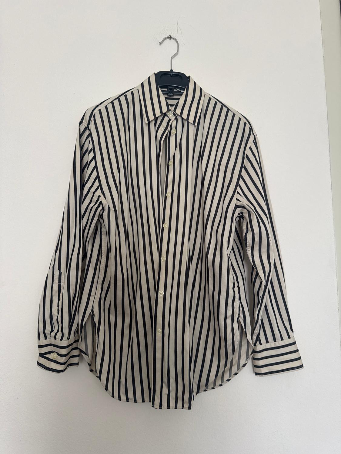 Black and white striped shirt hanging on a black hanger against a white wall.
