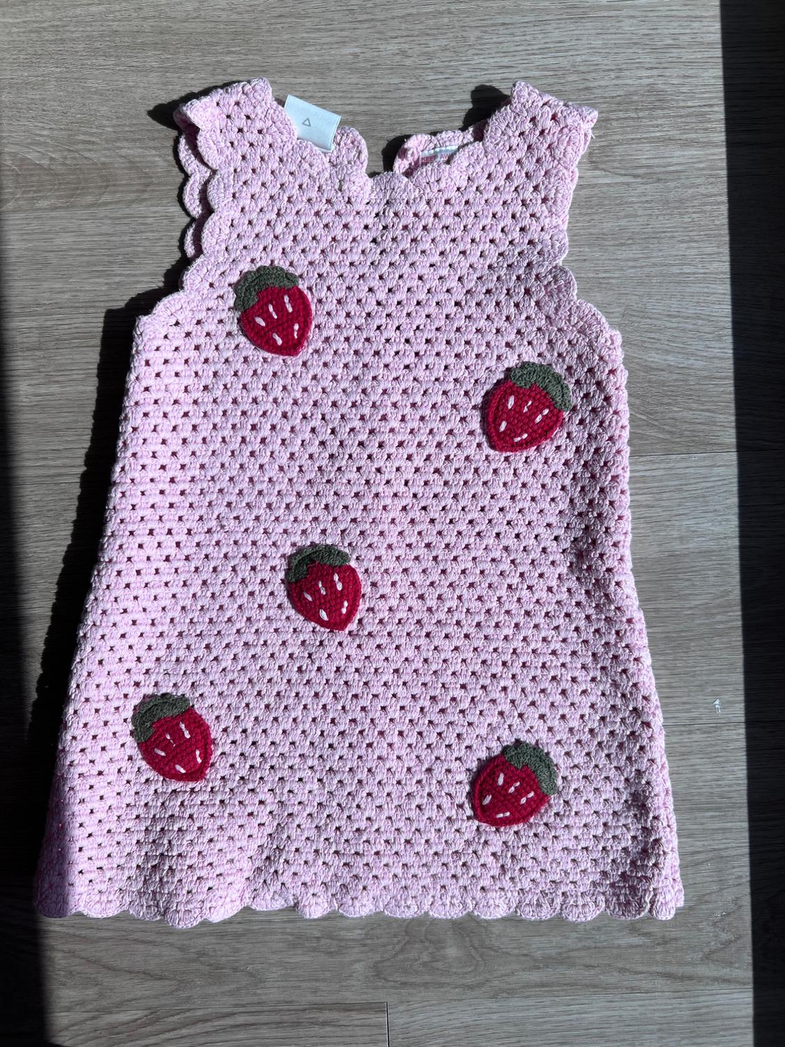 Pink sleeveless crochet dress with red strawberry appliqués, on a wooden surface.