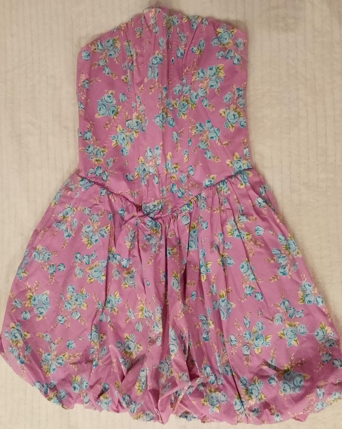 Pink strapless dress with a blue floral print. Fitted bodice and voluminous skirt design, set against a light background.