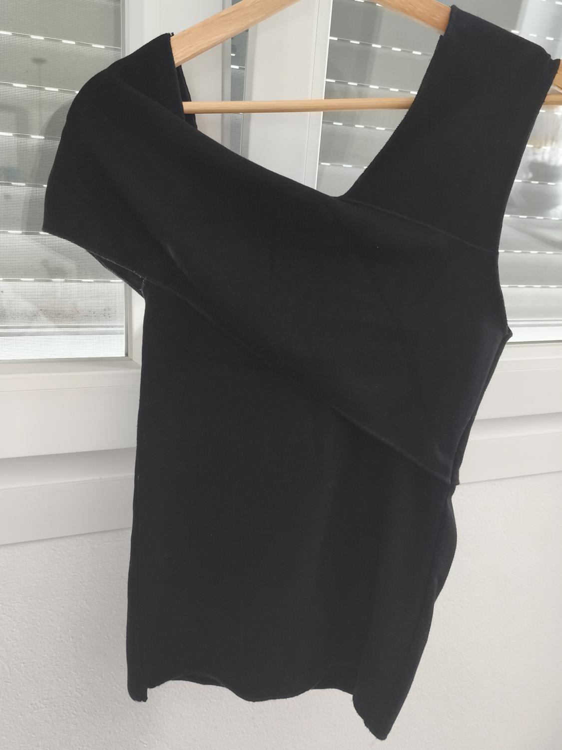 Asymmetric black top hanging on a wooden hanger in front of a window with white blinds.