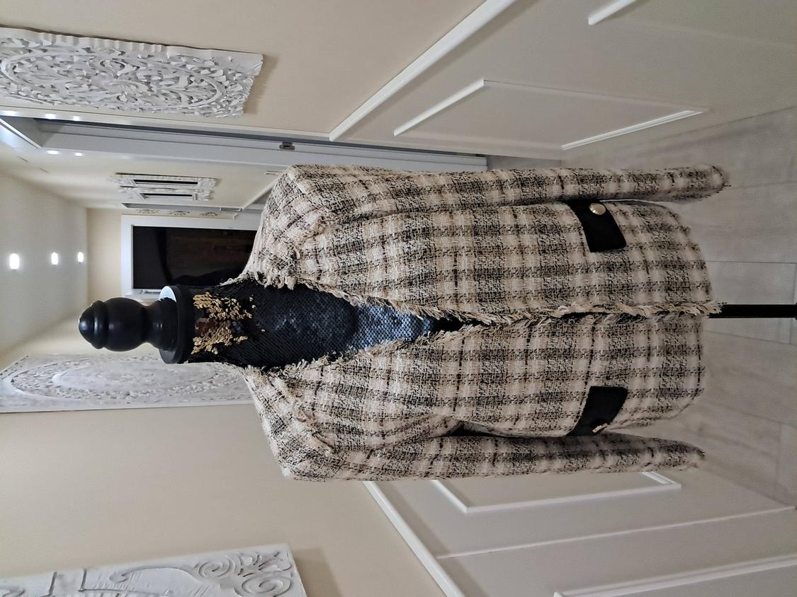 Mannequin in a beige and black checked jacket in a hallway with white wall decor.