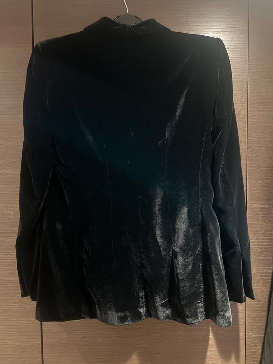 Black velvet jacket hanging on a hanger, viewed from behind, against a brown wooden background.