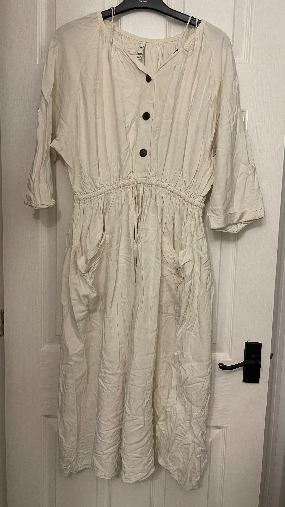 Creased white dress with dark buttons and three-quarter length sleeves, hanging on a white door.