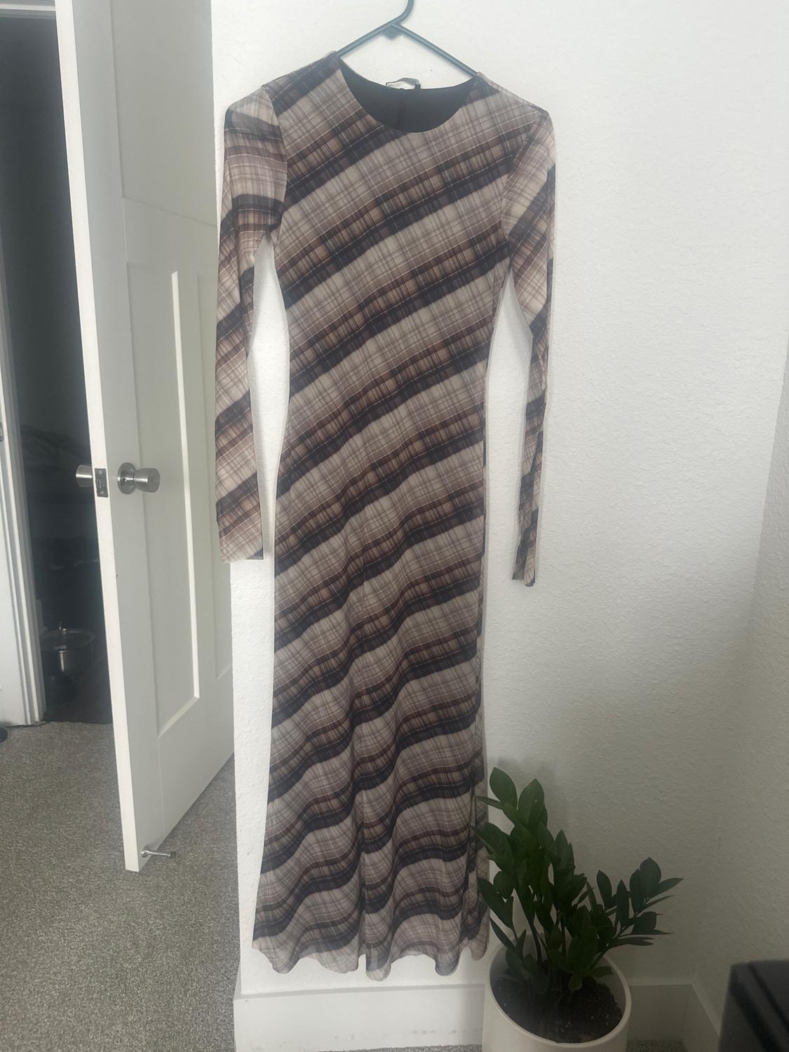Long-sleeved maxi dress with a diagonal check print in brown and beige tones, hanging on a white hanger.