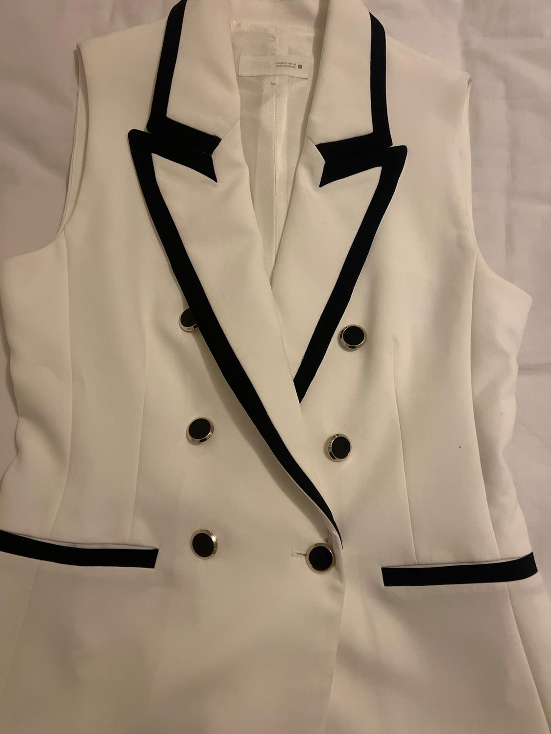 White sleeveless waistcoat with black lapels and gold buttons on a white background. Elegant and modern design.