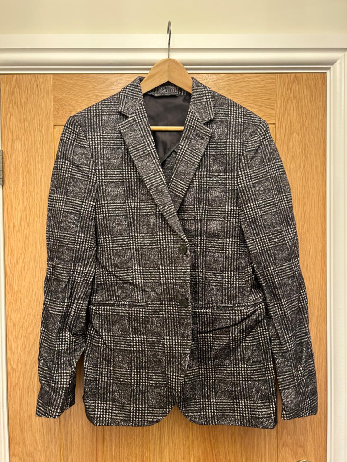 Front view of a grey and black checked jacket with lapels and side pockets.