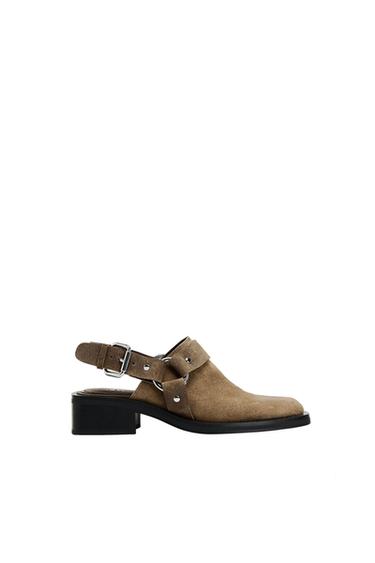 Brown suede slingback shoe with a low black heel, strap with buckle and silver metallic details on a white background.