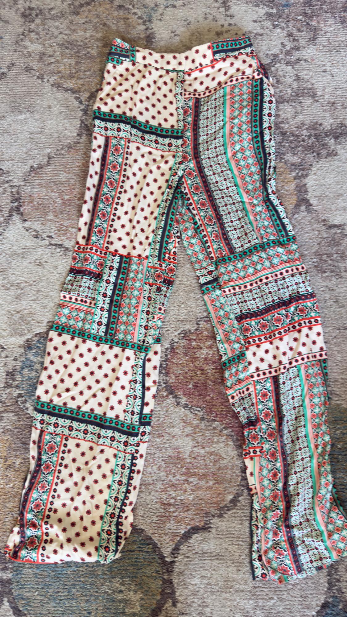 Printed pants with geometric and floral patterns in red, green, and black on a beige background, placed on a textured rug.