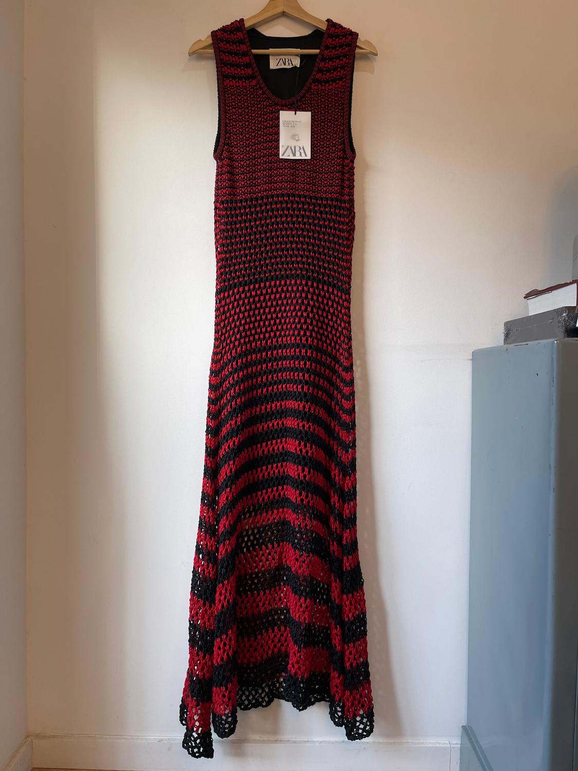 Red and black knitted dress hanging on a wooden hanger, with Zara label visible at the neck. White background.