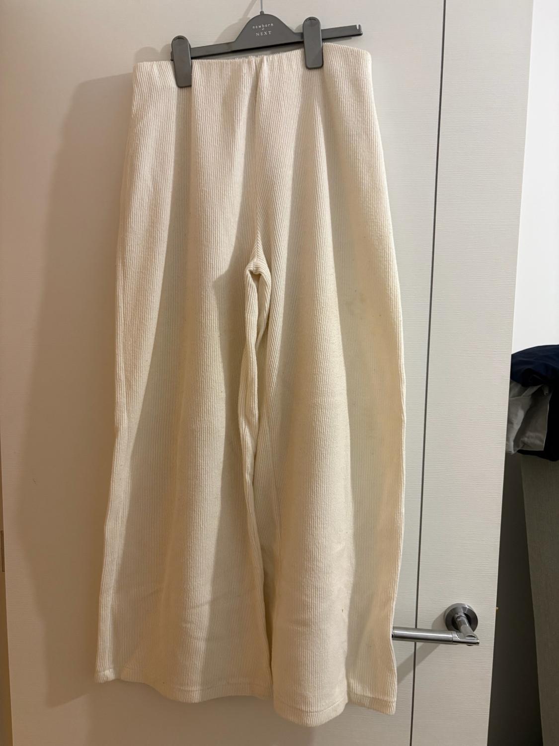 Cream wide-leg ribbed trousers in cream hanging on a coat hanger over a white door. Text: newborn NEXT.