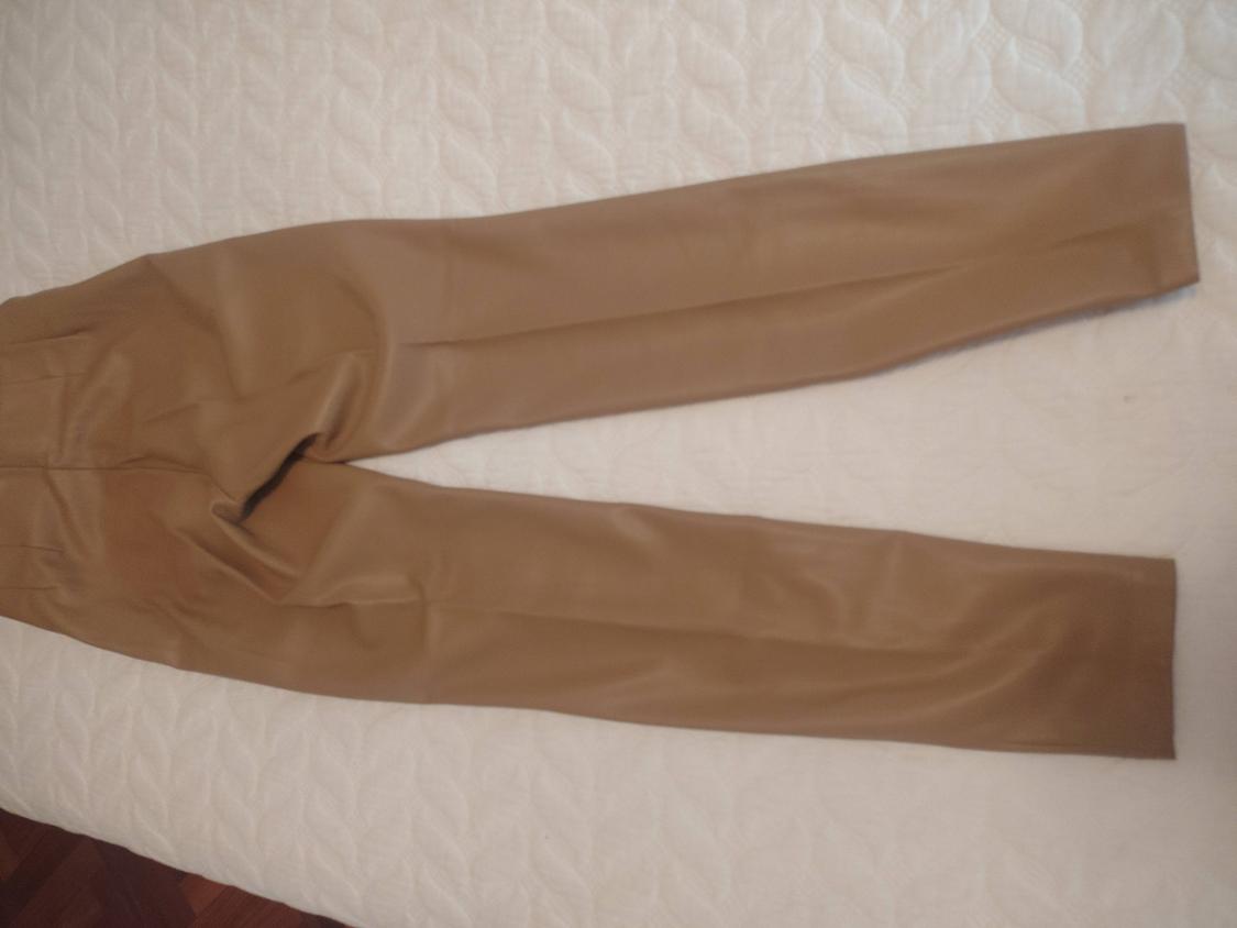 Brown plain fabric trousers laid out on a textured white bedspread.