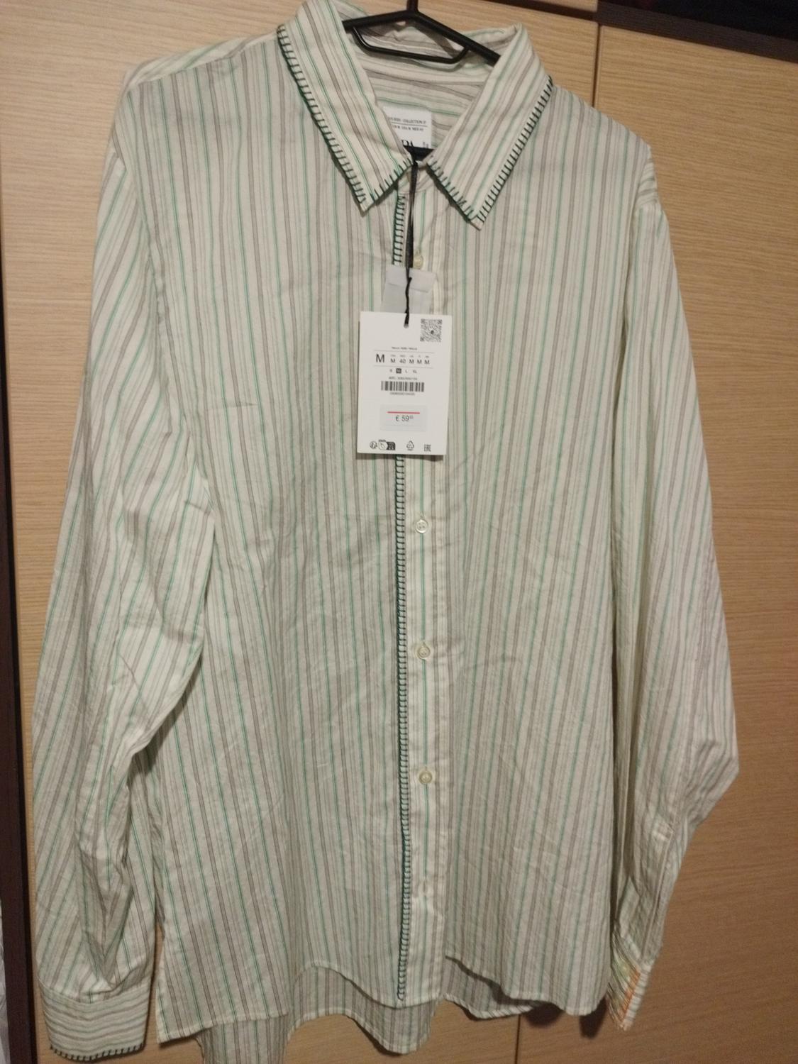 Green and white striped shirt hanging on a hanger, with a visible price tag of £5.99. Light wooden background.