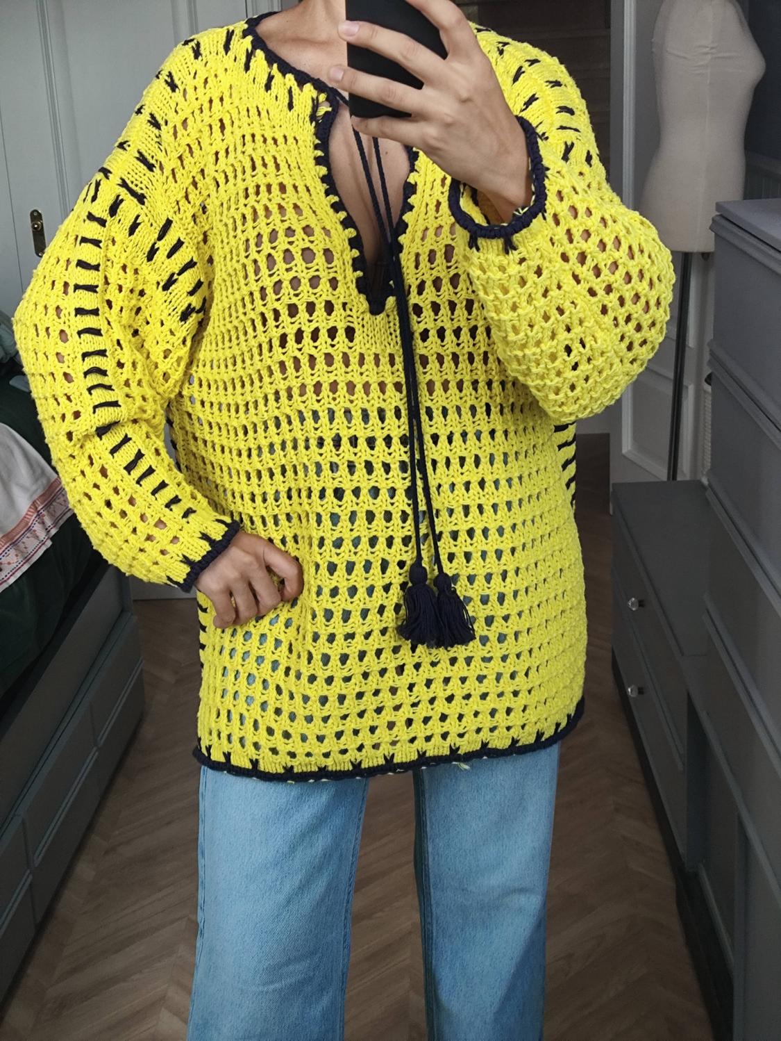 Mirror selfie of a person in a yellow open-knit jumper with dark trim and tassels, paired with blue jeans.