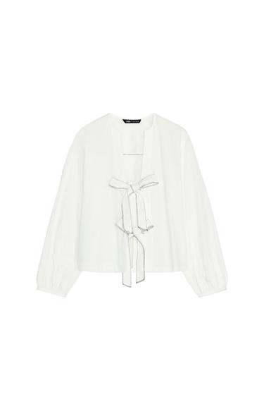 Front view of a white blouse with decorative bow detail on the front and long sleeves.