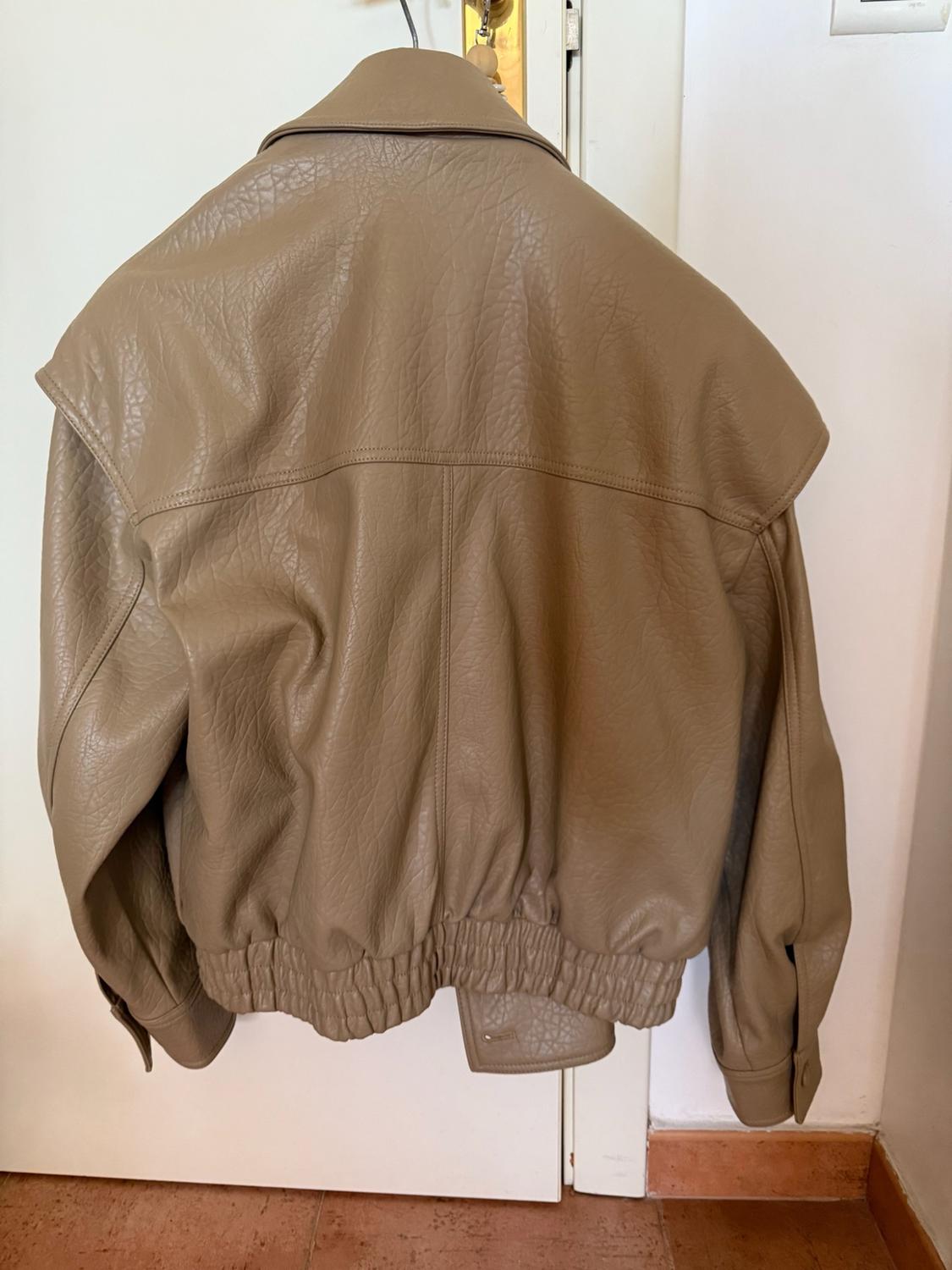 Rear view of a textured beige jacket hanging on a white door above a tiled floor. Its gathered elasticated hem stands out.