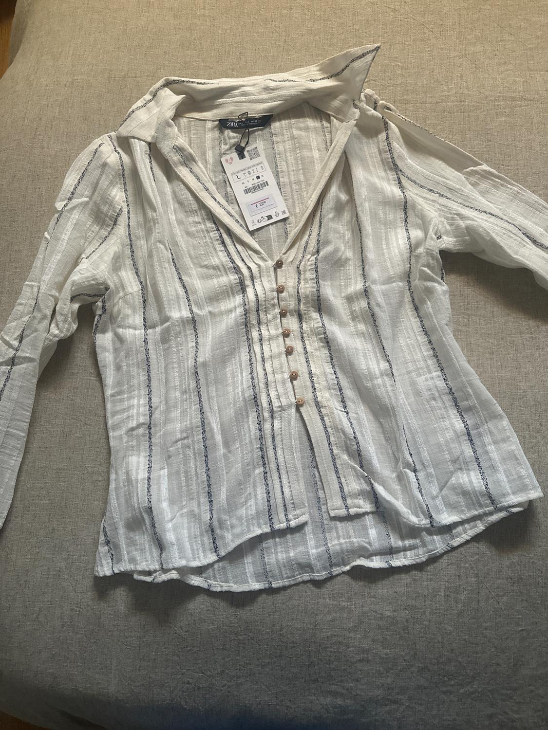 White shirt with blue stripes and brown buttons on a beige surface. Visible label with a price of €17.99.