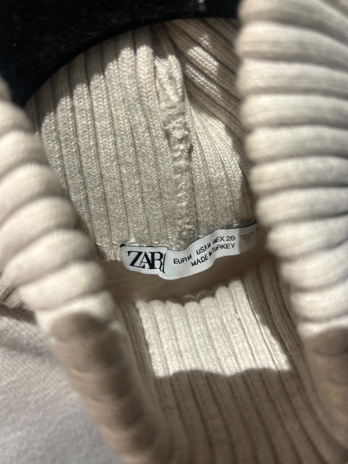 White clothing label with text "ZARA EUR M USA M MEX 28 MADE IN TURKEY" on a ribbed knit fabric, close-up view.