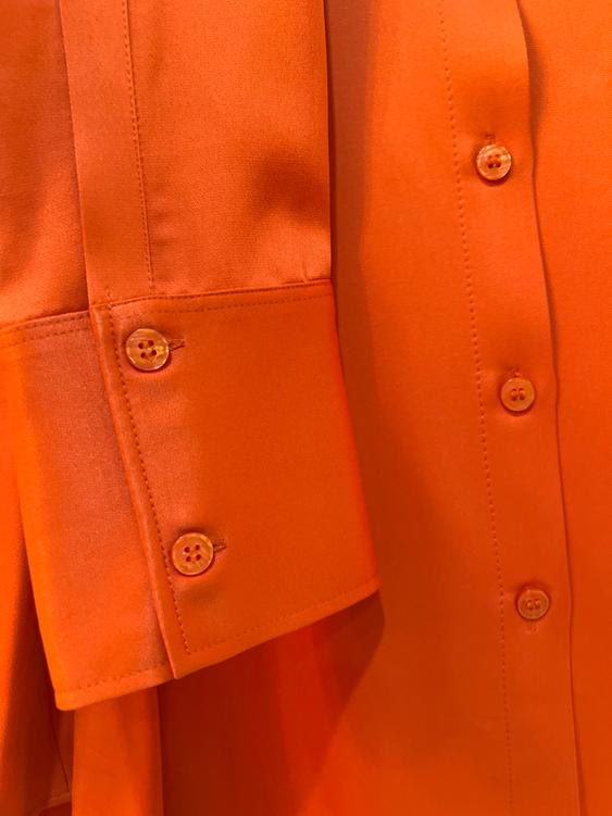 Orange satin fabric shirt with same-color buttons. Cuff detail with double button and visible seams.