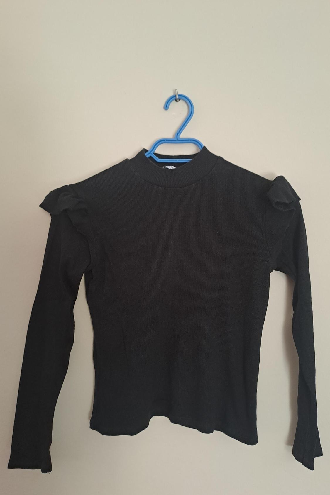 Front view of a black jumper with frills on the shoulders and a round neck.