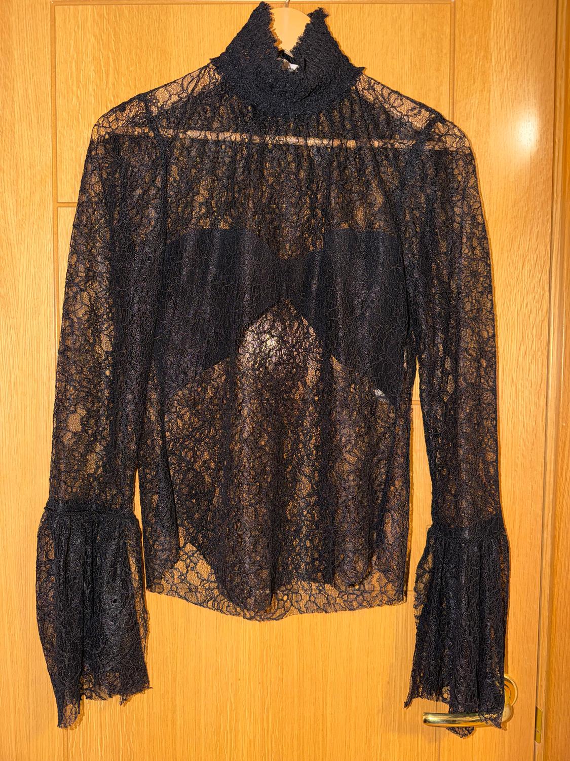 Black lace blouse with a high neck and long, flared sleeves, hanging on a light wooden door.