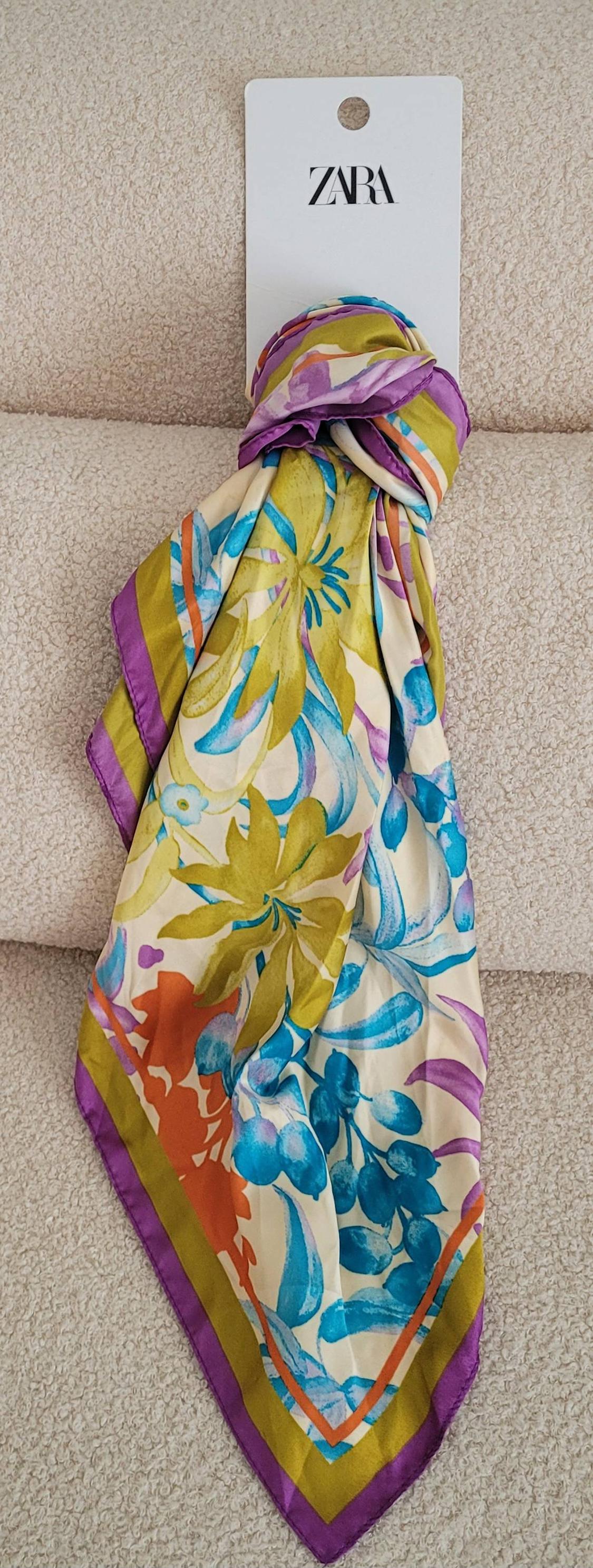 Silk scarf with a floral print in shades of green, blue, and purple, hanging from a white tag with the Zara logo.