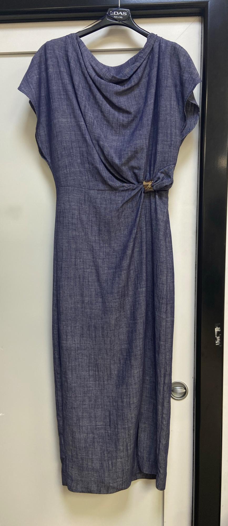 Blue dress with a draped neckline and waist detail, hanging on a white door. Text on the hanger: E-DAS Made in Italy.